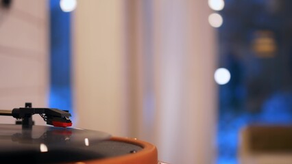A close-up of a record spinning in a player, in the background lights in a beautiful bokeh. Retro music and classical music from vinyl records are listened to at home.