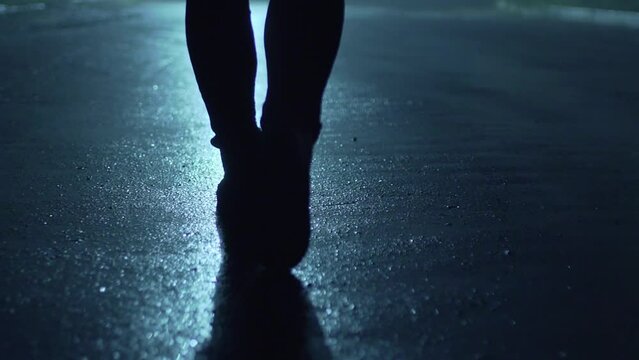 Legs of a man in backlight walking down the street at night.