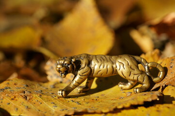 Metal tiger figurine on the background of autumn leaves.