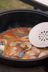 Pieces of mackerel with vegetables are cooked in a cast-iron cauldron. Cooking outdoors. Close-up.
