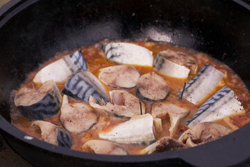 Pieces of mackerel with vegetables are cooked in a cast-iron cauldron. Cooking outdoors. Close-up.