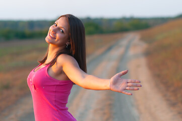 Young smiling woman walking on the road in the nature on a sunny summer day