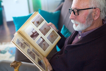 Senior man looking at photos in photo album with photographs from his childhood