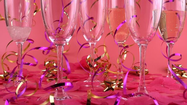 Pouring sparkling wine into glasses on a pink background with confetti in the form of hearts and serpentine.