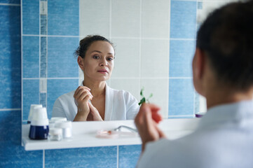 Reflection in the bathroom mirror of a serene woman massaging her hands soaked in moisturizer, caring for her hands skin