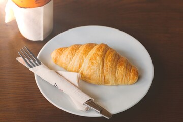 The croissant is placed on a plate with a knife and fork with a drink on the side