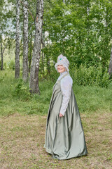 Naklejka premium Smiling caucasian senior woman in stylized Russian traditional sundress and headdress, at rural.