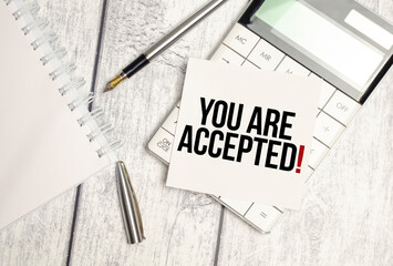 Text YOU ARE ACCEPTED on paper card and calculator on wooden background