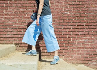 A girl in blue culottes and sneakers climbs the stairs outside on a sunny summer day. Selective...