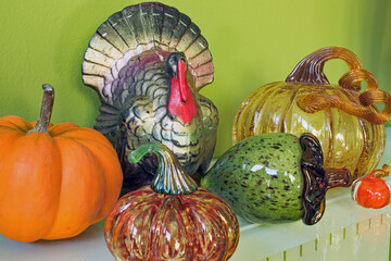 A mantle display for autumn with an acorn and pumpkins in various media, and a turkey candle.