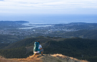 Fototapeta premium Sitting hiker at sunset contemplating the city and the sea