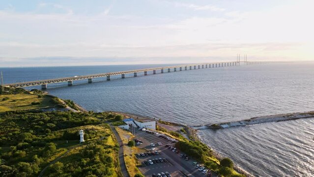 Aerial view of Oresund bridge at the sunset in summer. Cinematic shot a shore and bridge between Sweden and Denmark. Oresund bridge with a parking at the shore. High quality 4k footage