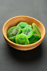 Wooden bowl with several slices of dry kiwi fruit on a dark concrete background, close-up