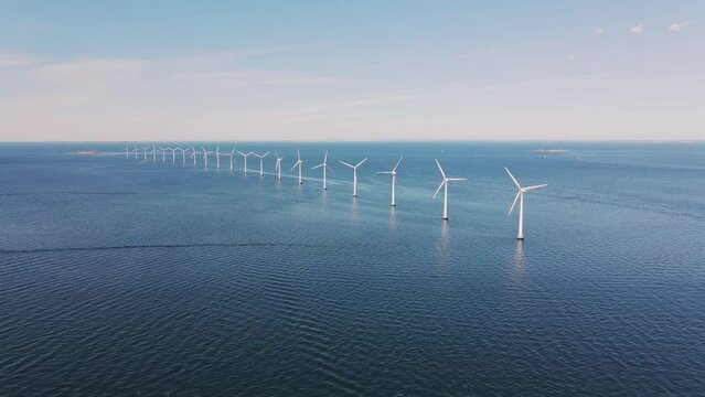 Drone flies over an offshore windmill row in the ocean. Windmills factory in Sweden. Green energy and protection of the environment. Blue ocean and sky. High quality 4k footage