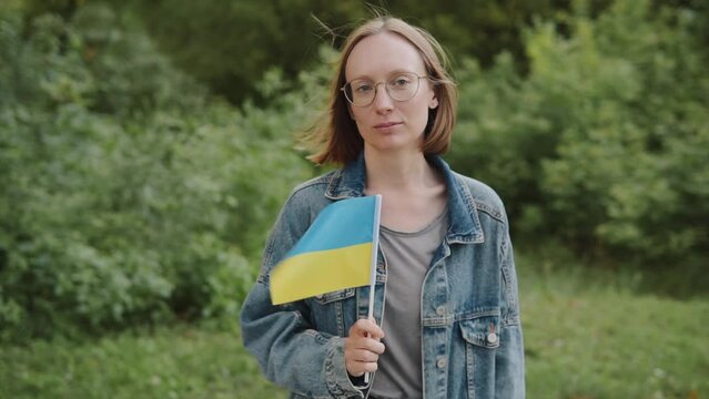 Young woman activist with the flag of Ukraine on the street looks at the camera. 