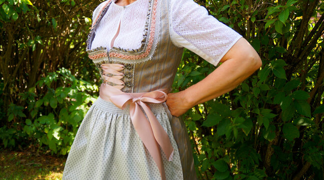a woman wearing a beautiful luxury traditional Bavarian or also Austrian dirndl dress (also called Tracht) and a gorgeous white lace blouse on a sunny summer day (Munich, Bavaria, Germany)