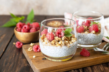 Healthy breakfast menu concept. Home made granola breakfast. Glass of parfait made of granola, berries raspberry, yogurt with chia seeds on rustic table. Copy space.