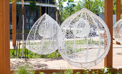 A cozy seating area in the yard of a modern residential complex with wooden benches, hanging white...