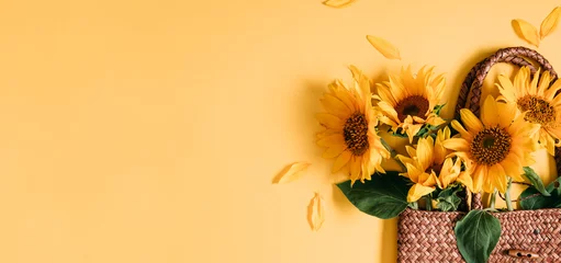 Foto op Aluminium Summer or autumn background. Wicker bag with bouquet of sunflower flowers on yellow background. Flat lay, top view, copy space © prime1001