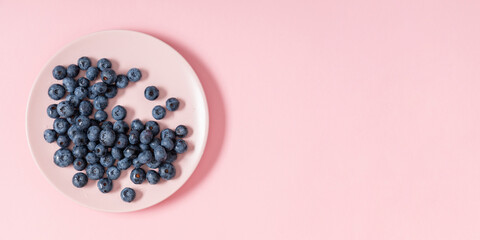 Blueberries on pink background. Juicy fresh blueberries on pink plate on table. Flat lay, top view, copy space