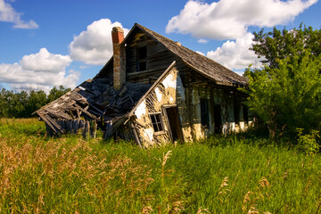 Old and weathered abandoned farm house against a blue sky with fluffy clouds