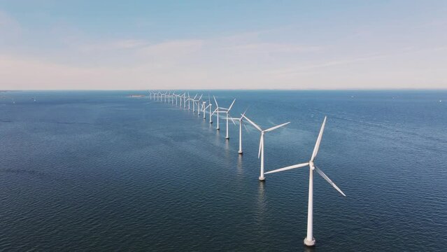Drone flies over an offshore windmill row in the ocean. Windmills factory in Sweden. Green energy and protection of the environment. Blue ocean and sky. High quality 4k footage