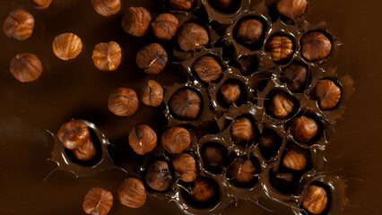 Super Slow Motion of Falling Hazelnuts into Dark Hot Melted Chocolate, Close-up, Top Shot.