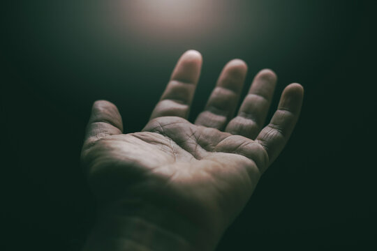 Detail shot of the palm of a man's hand facing upwards lit from above that connotes serenity and spirituality