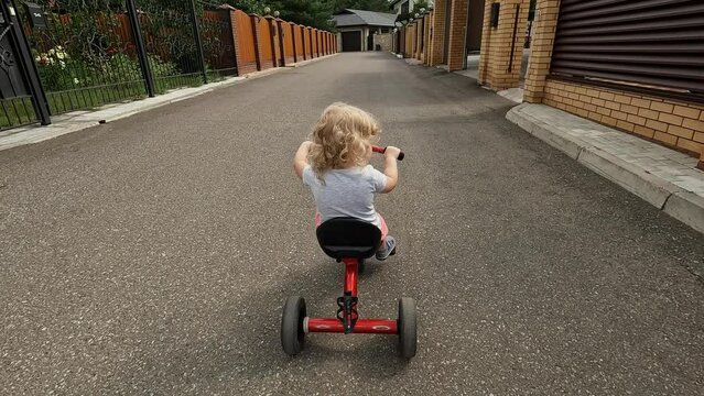 Happy little baby boy girl riding on three wheel red bike back view steadicam establish shot