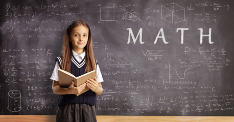 Schoolgirl with a book standing in front of a chalkboard with math formulas