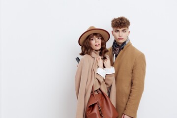 a stylish, loving couple, a man with and a woman are standing on a white background in an autumn coat, a woman has a hat on her head and she is holding a brown bag