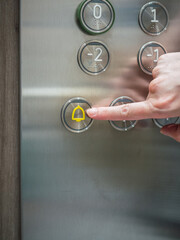 Woman's hand pressing the alarm button inside the elevator