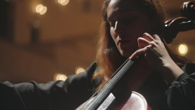 portrait of beautiful emotional female violoncellist on scene of opera house, woman is playing cello
