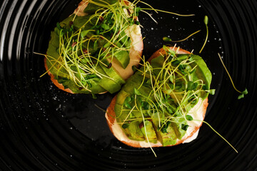 Obraz premium croutons with avocado and microgreens on a black plate top view close-up