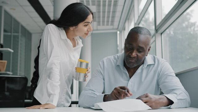 Arab businesswoman team leader explain marketing documentation report to african american colleague. Diverse multiracial co-workers two business people in office discuss documents corporate education