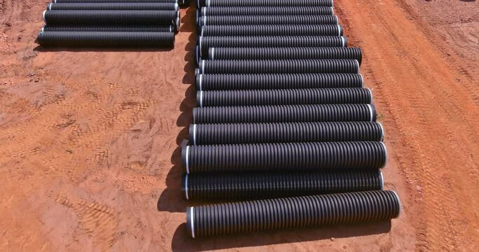 In order to build a drain system on construction site, PVC new black plastic pipes are stacked in rows for new home