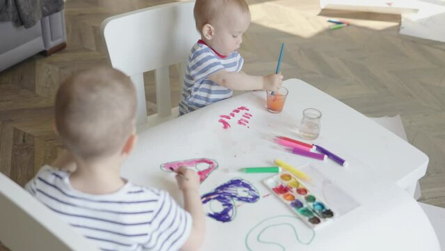 two little sibling brothers toddlers painting abc alphabet letters indoor home living room. concept early education developing art skills, imagination, leisure activities preparing to school days