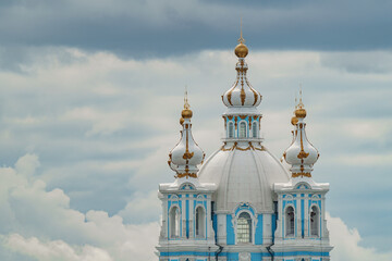 Fototapeta na wymiar golden domes and crosses of the Smolny Cathedral in sunny weather against the background of a gloomy sky