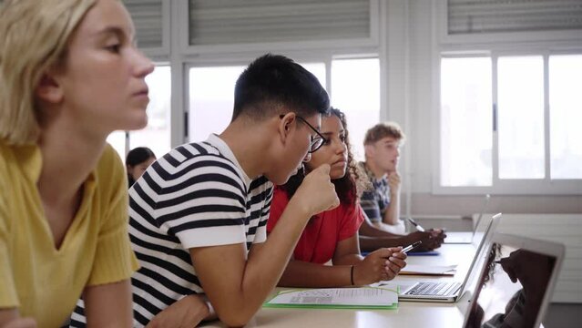High school classroom: A boy and girl using a laptop computer while attending to the teacher in class. Group of students learning in the classroom.