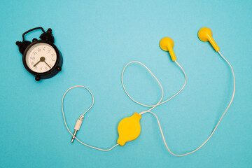 Black alarm clock and yellow headphones on a blue background. Music time. View from above.