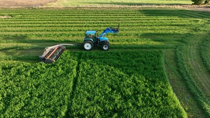 Aerial farmer cutting alfalfa hay tractor harvest. Rural farming community agricultural economy. Summer harvesting of alfalfa hay agriculture. Tractor equipment, green field. Mountain Valley.