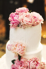 Multilevel wedding cake on the table decorated with peonies