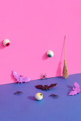 Creative halloween scene with eye ball, spider, bat and broom. Vibrant bold colors. Neon pink and...