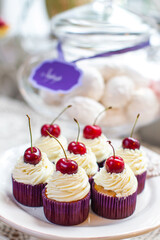 Muffins on a plate decorated with cream and cherries