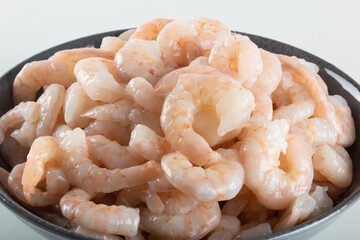 A bowl of peeled fresh raw white shrimp with tail.