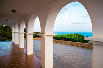 The sea can be seen from the top of a hill, through the traditional white arches of the Mediterranean houses.