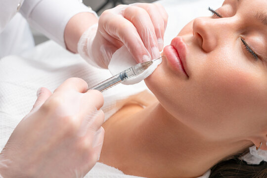 Lip augmentation and correction procedure in a cosmetology salon. The specialist makes an injection in the patient's lips.