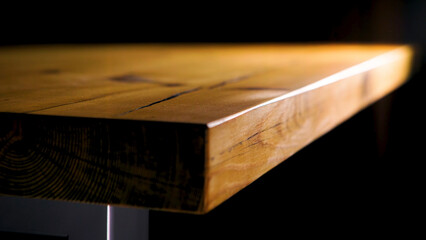 Close-up of edge of wooden table on dark background. Stock footage. Beautiful smooth edge of brown wooden table lit by warm light on dark background