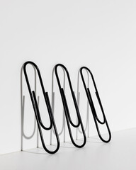 three large black paper clips leaning on white wall with shadows