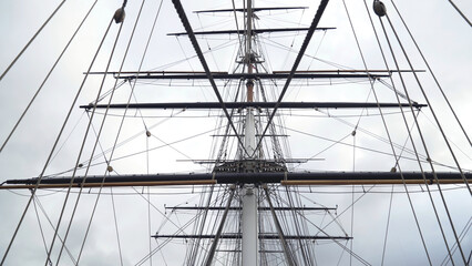 Masts and cables of ship on background of cloudy sky. Action. Towering masts with many intertwined...